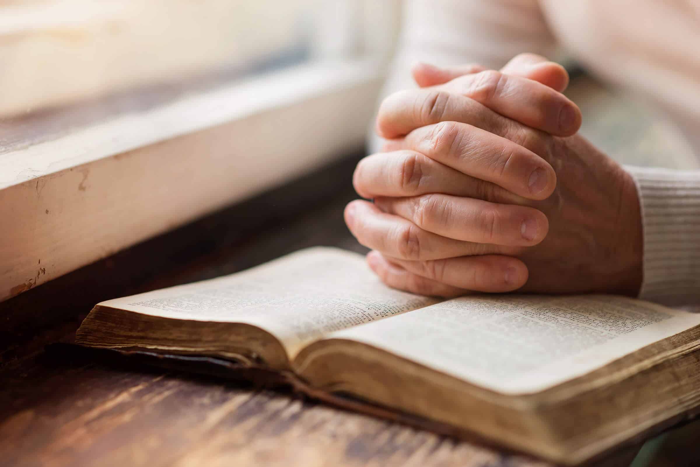 Decorative header featuring a pair of female hands clasped in prayer resting on an open Bible.